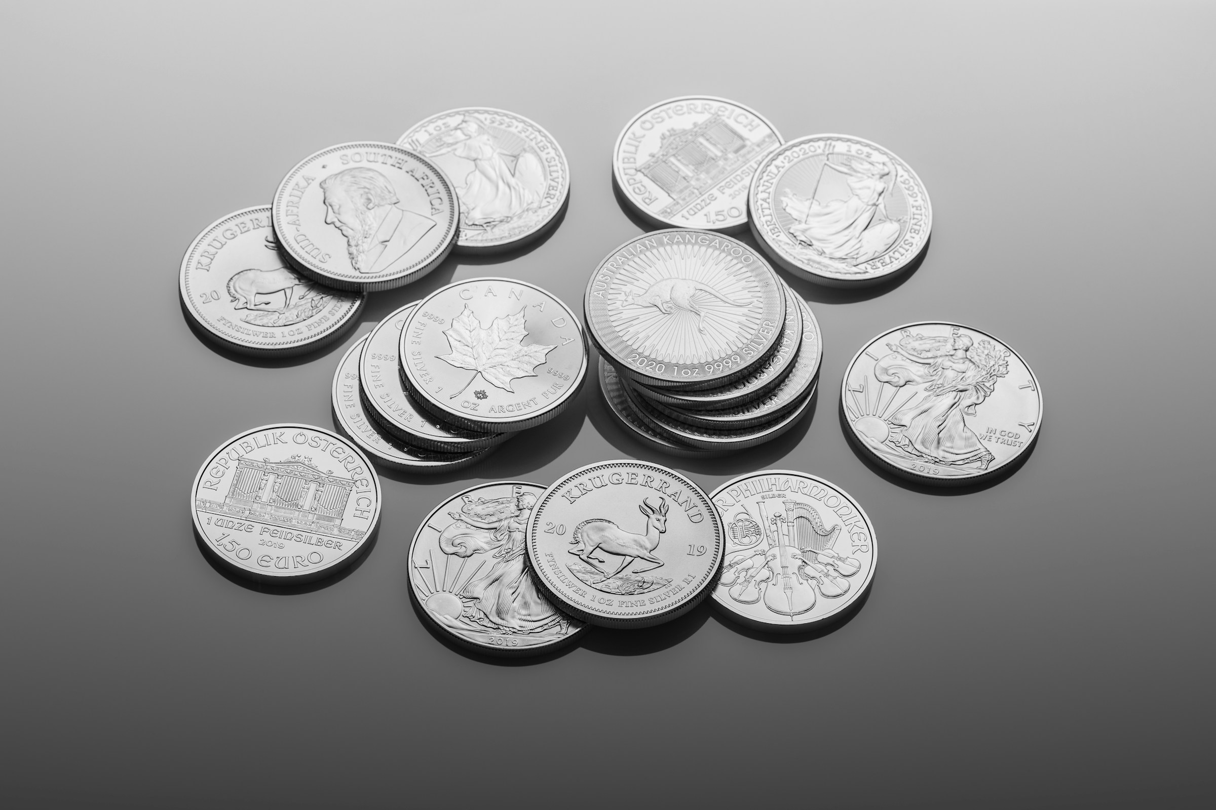 A monochrome close-up of silver coins scattered and stacked across a smooth, reflective surface.